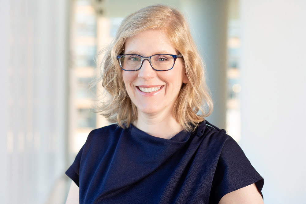 portrait of Holly J. Morris, a blonde with blue eyes, glasses and wavy hair.
